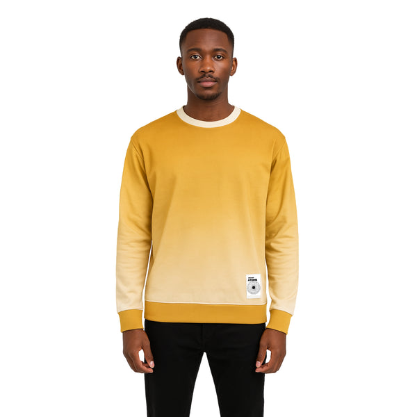 Model wearing Breakin' Atoms "Brown Autumn Sweater," a crewneck sweatshirt with a soft ombré fade from warm golden brown to off-white, finished with a woven logo patch — the perfect blend of cozy and stylish for fall layering.