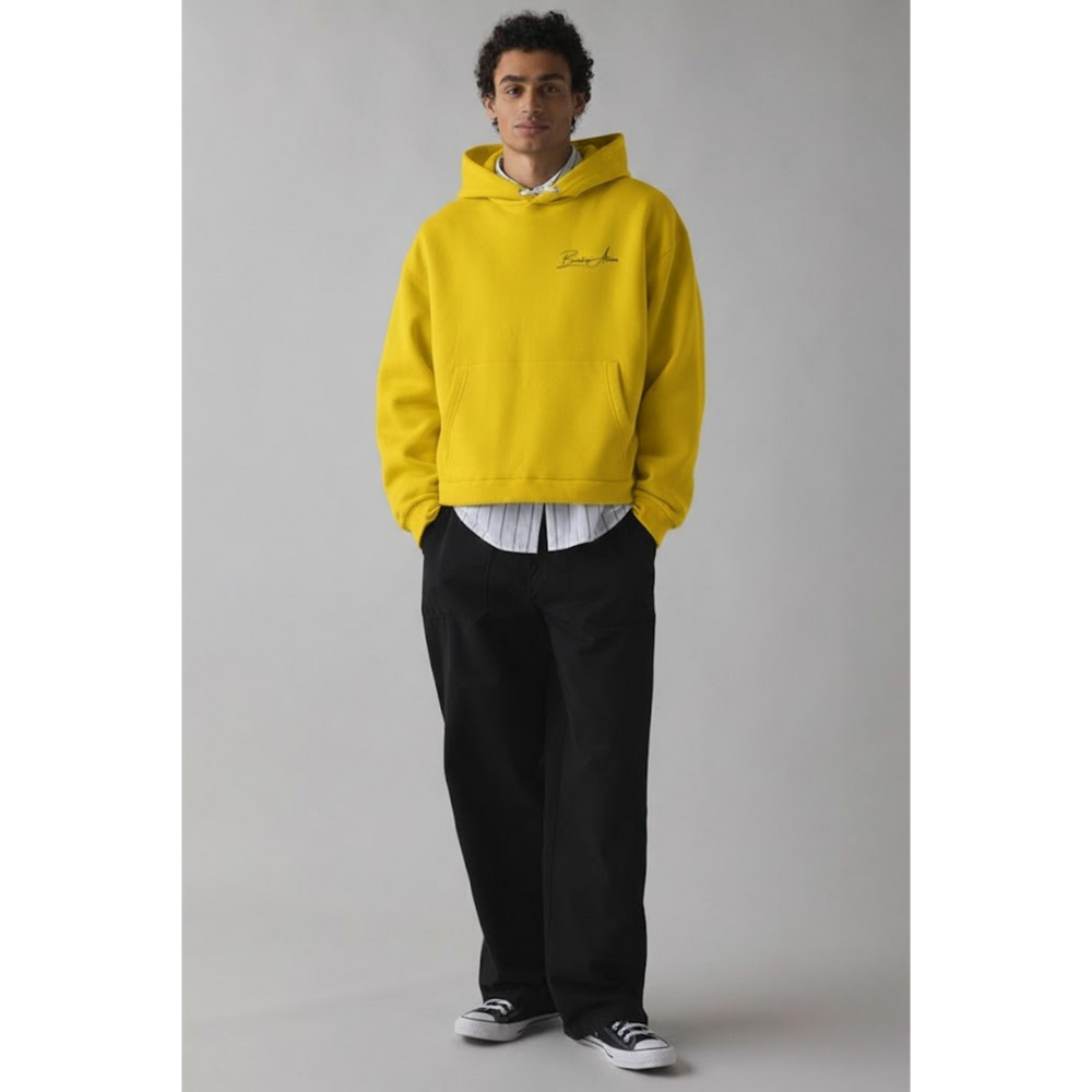 Breakin’ Atoms YeYellowLightShiftSweaterr in bright yellow, relaxed-fit pullover hoodie with drawstring hood, kangaroo pocket, ribbed cuffs and hem, and small tonal Breakin’ Atoms script logo on the left chest, shown on-model in a studio setting. — Breakin Atoms premium streetwear