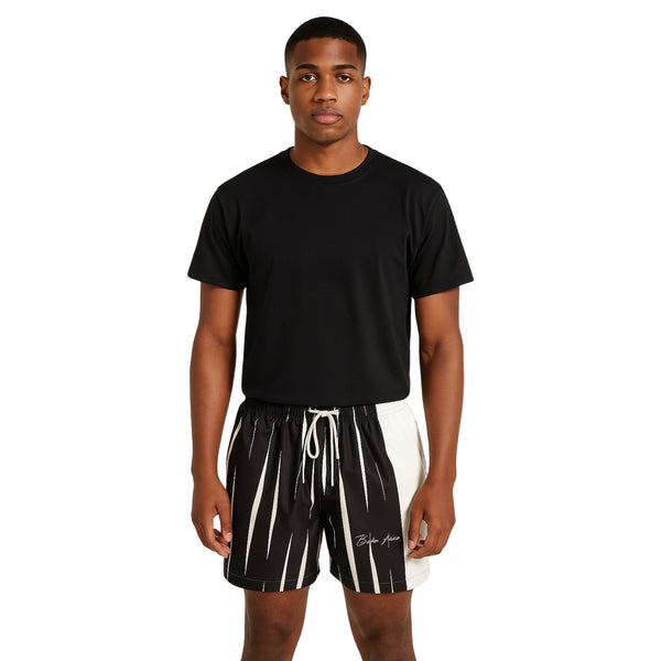 Model wearing Breakin' Atoms "Monochrome Strike Shorts," black and white split-panel shorts with vertical stripe detailing and signature branding — combining clean minimalism with sharp streetwear edge.