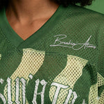 Close-up of Breakin’ Atoms WaveFront 21 green mesh jersey showing ribbed V-neck collar, perforated fabric, and white signature logo on chest. thumbnail 2