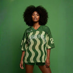  Full-length view of a model wearing the Breakin’ Atoms WaveFront 21 green mesh V-neck jersey with cream wave pattern, oversized fit, and “21” sleeve numbering. thumbnail 1