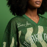 Angled close-up of the Breakin’ Atoms WaveFront 21 jersey highlighting dark green perforated mesh, ribbed V-neck, cream wave graphics, and white chest logo thumbnail 3